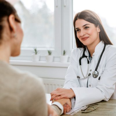 Friendly female doctor holding female patient's hand for encouragement and empathy.